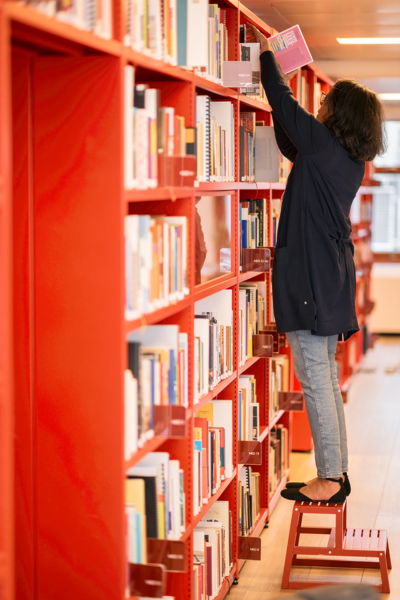 Medewerker zoekt boeken in de Atria-boekenkast